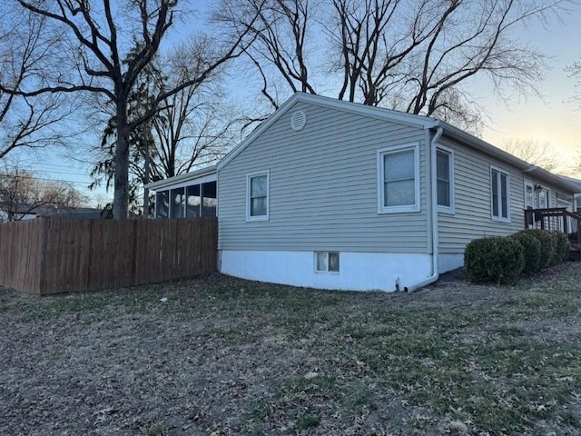 property exterior at dusk with a carport, fence, a lawn, and a sunroom