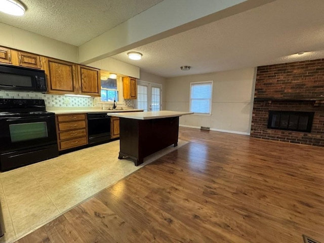 kitchen with brown cabinetry, a fireplace, black appliances, light countertops, and open floor plan