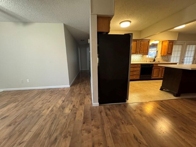 kitchen featuring freestanding refrigerator, light countertops, light wood-style floors, dishwasher, and brown cabinets