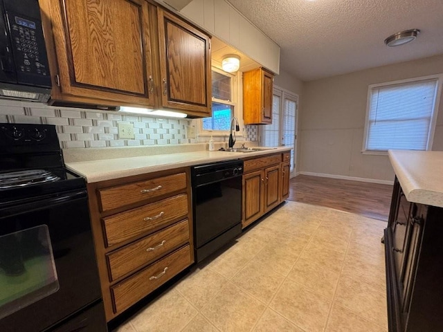 kitchen with black appliances, light countertops, brown cabinets, a textured ceiling, and a sink