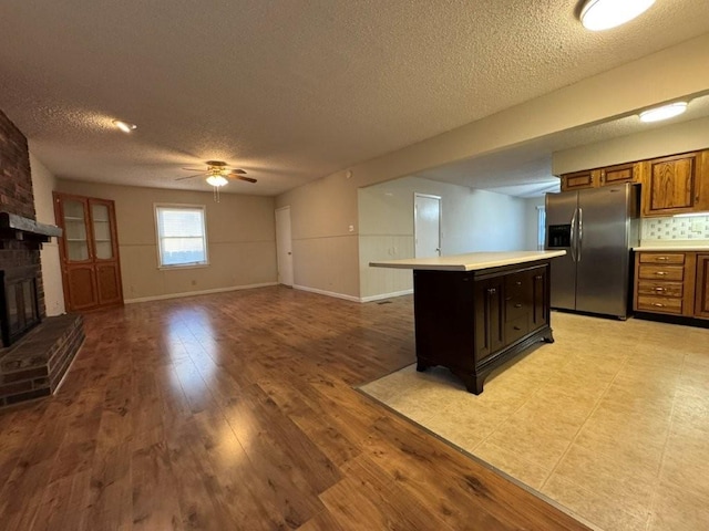 kitchen with a fireplace, light wood finished floors, stainless steel fridge with ice dispenser, decorative backsplash, and light countertops