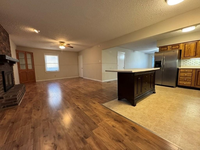 kitchen featuring stainless steel fridge with ice dispenser, light countertops, light wood-style floors, a brick fireplace, and brown cabinets