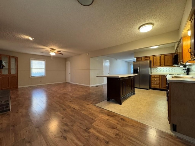 kitchen with light wood finished floors, a kitchen island, light countertops, and stainless steel refrigerator with ice dispenser