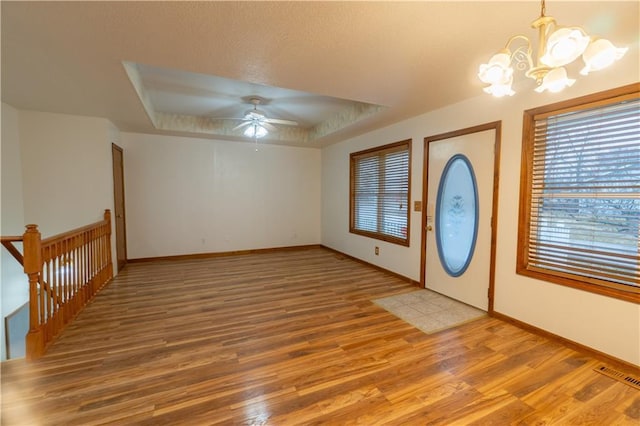 entrance foyer featuring visible vents, baseboards, light wood-type flooring, ceiling fan with notable chandelier, and a raised ceiling