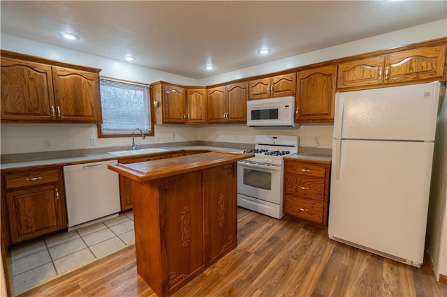 kitchen featuring brown cabinets, a sink, a kitchen island, white appliances, and light wood finished floors