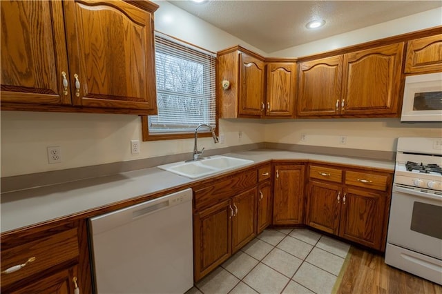 kitchen featuring light countertops, light tile patterned flooring, brown cabinetry, white appliances, and a sink