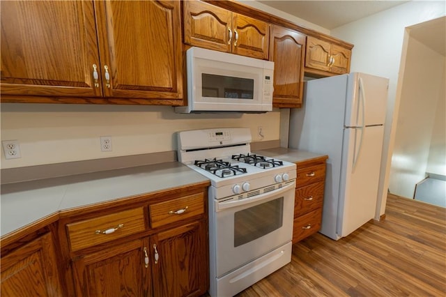 kitchen featuring brown cabinets, white appliances, light countertops, and wood finished floors