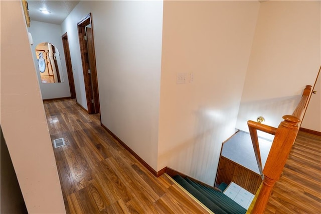 corridor featuring visible vents, baseboards, an upstairs landing, wood finished floors, and arched walkways