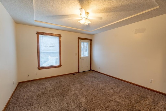 spare room featuring a ceiling fan, carpet, baseboards, a textured ceiling, and a raised ceiling