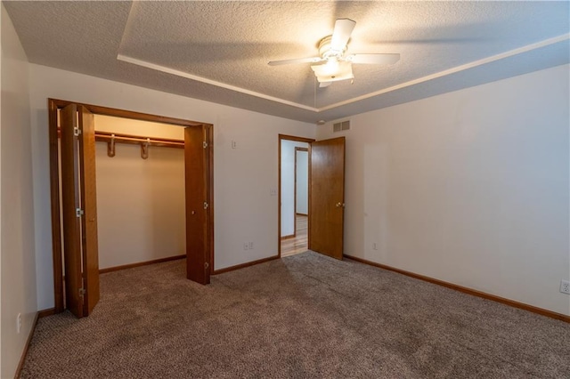 unfurnished bedroom featuring visible vents, a raised ceiling, a textured ceiling, carpet floors, and baseboards