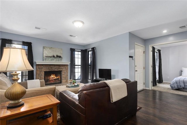 living area featuring a stone fireplace, visible vents, baseboards, and dark wood-style flooring