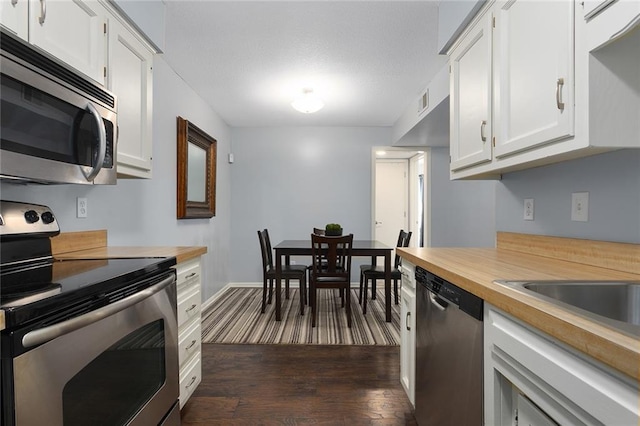 kitchen with dark wood-style floors, baseboards, appliances with stainless steel finishes, white cabinets, and wooden counters