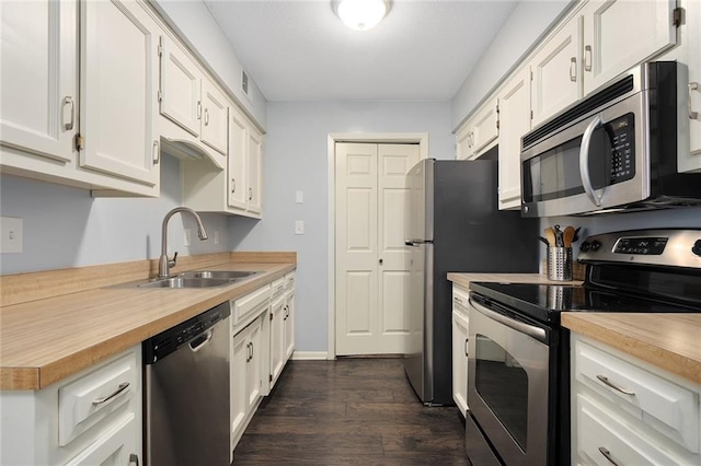 kitchen with butcher block countertops, dark wood-style floors, white cabinets, stainless steel appliances, and a sink