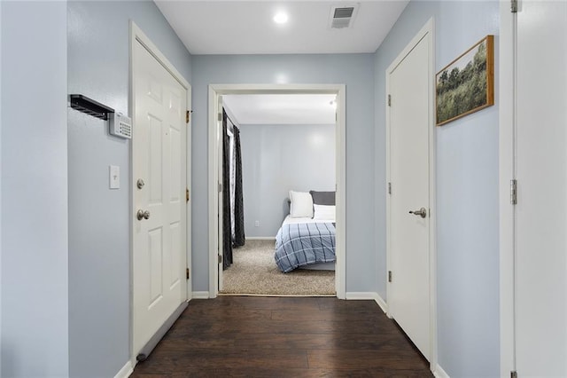 hallway with dark wood-style floors, visible vents, and baseboards