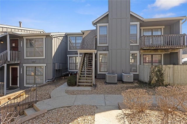 back of property with stairway, central AC unit, board and batten siding, and a shingled roof