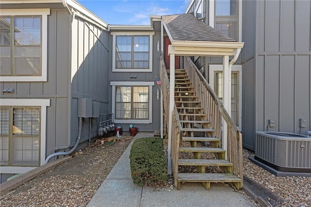 property entrance featuring central AC unit, board and batten siding, and a shingled roof