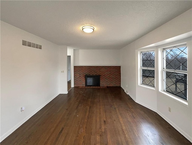 unfurnished living room with visible vents, a brick fireplace, a textured ceiling, and wood finished floors