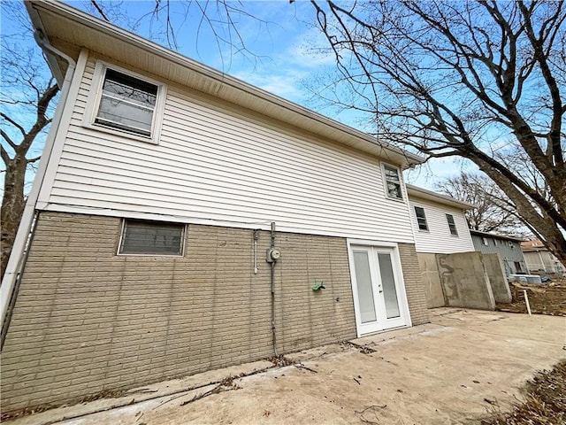 view of side of home featuring french doors, brick siding, and a patio area