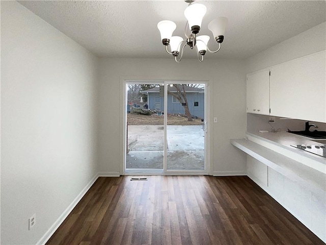 unfurnished dining area with dark wood finished floors, a notable chandelier, visible vents, and baseboards