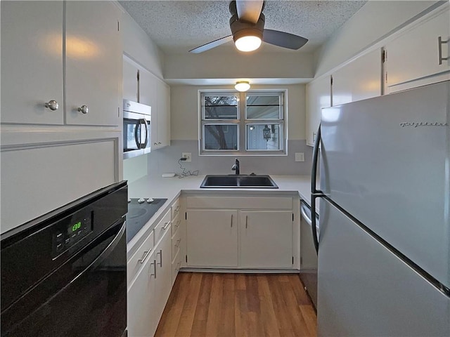 kitchen with dark wood-type flooring, black appliances, a sink, a textured ceiling, and white cabinets