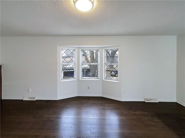 unfurnished room featuring visible vents, baseboards, a textured ceiling, and dark wood-style flooring