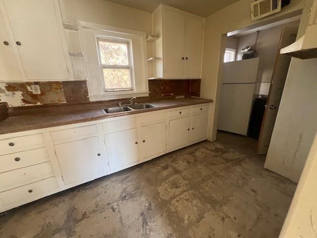 kitchen with tasteful backsplash, white cabinets, freestanding refrigerator, and a sink