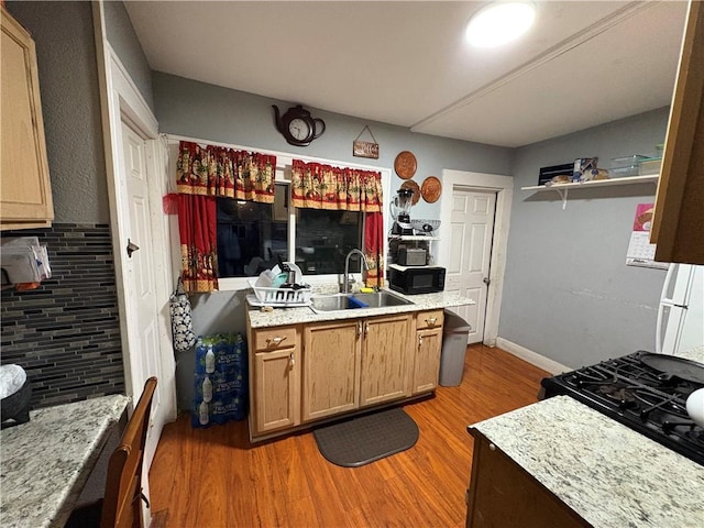 kitchen featuring light stone counters, light wood-style flooring, a sink, black appliances, and tasteful backsplash