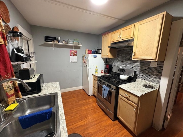 kitchen featuring under cabinet range hood, a sink, freestanding refrigerator, gas stove, and light wood-style floors