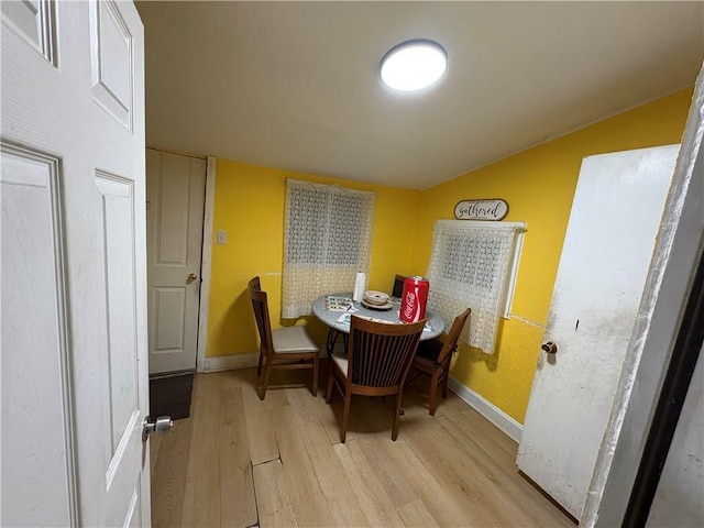 dining space featuring light wood finished floors, lofted ceiling, and baseboards