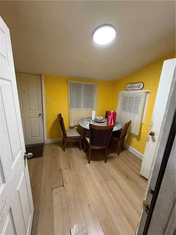 dining room featuring lofted ceiling, baseboards, and light wood finished floors