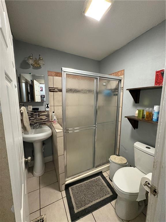 bathroom featuring tile patterned flooring, a shower stall, and toilet