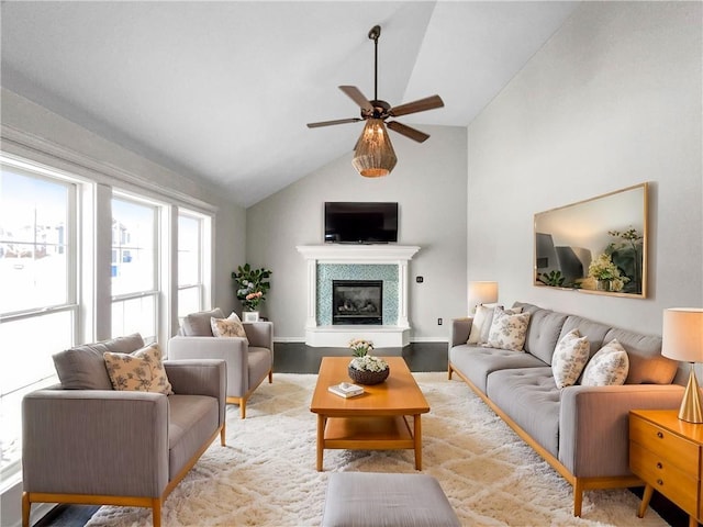 living area with light wood finished floors, baseboards, ceiling fan, a tiled fireplace, and vaulted ceiling