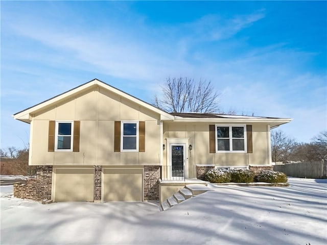 raised ranch with a garage, fence, brick siding, and stucco siding