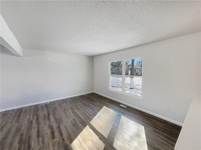 unfurnished room with visible vents, baseboards, a textured ceiling, and dark wood-style floors