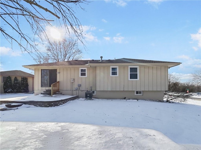 snow covered house featuring cooling unit and board and batten siding