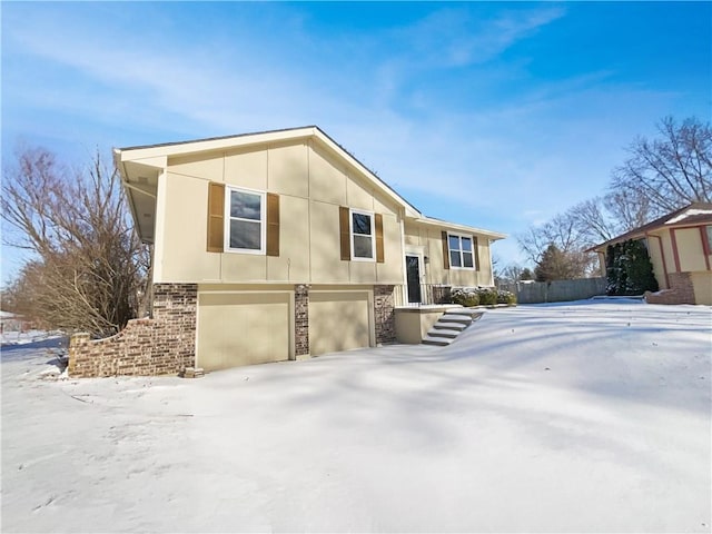 view of snow covered exterior featuring stucco siding, brick siding, and an attached garage