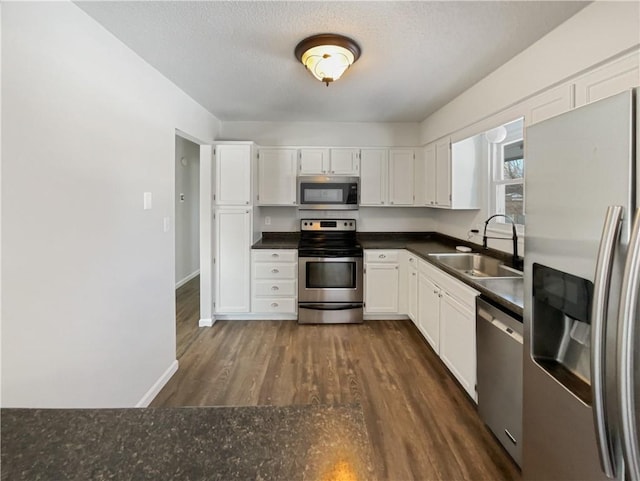 kitchen featuring dark countertops, white cabinets, appliances with stainless steel finishes, and a sink