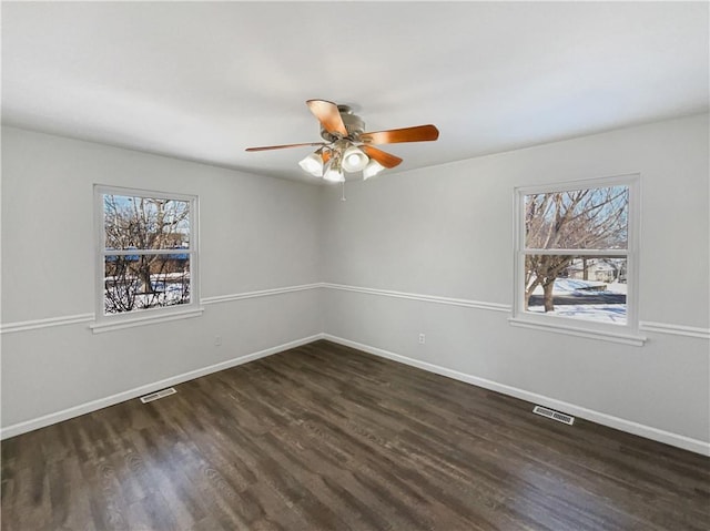 spare room featuring dark wood-type flooring, baseboards, visible vents, and a wealth of natural light