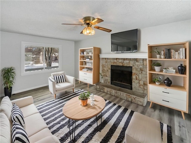 living area featuring ceiling fan, a textured ceiling, wood finished floors, and a fireplace