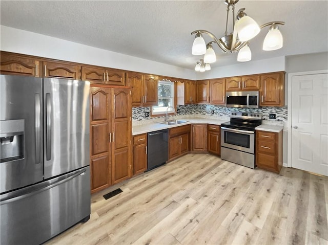 kitchen with light countertops, decorative backsplash, brown cabinets, appliances with stainless steel finishes, and light wood-style floors