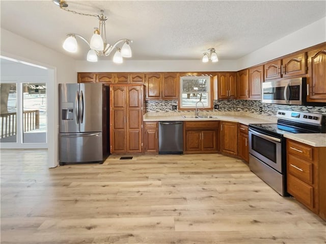 kitchen with brown cabinetry, a sink, stainless steel appliances, a notable chandelier, and tasteful backsplash