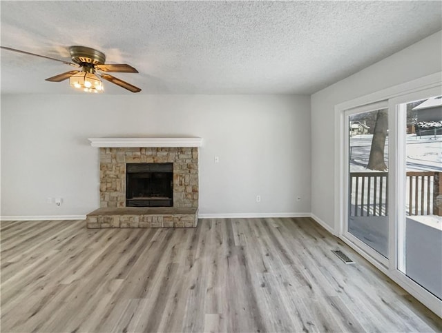 unfurnished living room with a stone fireplace, wood finished floors, visible vents, and baseboards