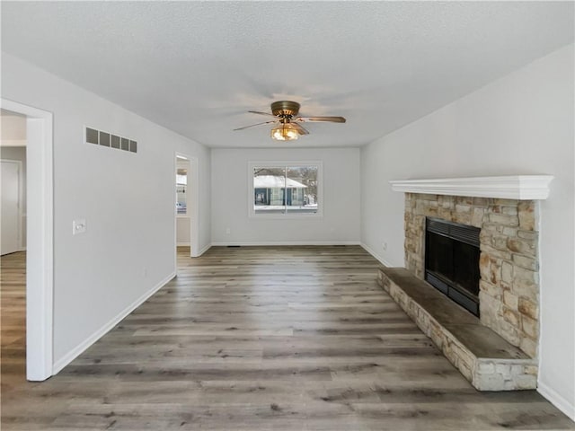 unfurnished living room with visible vents, ceiling fan, a fireplace, wood finished floors, and a textured ceiling