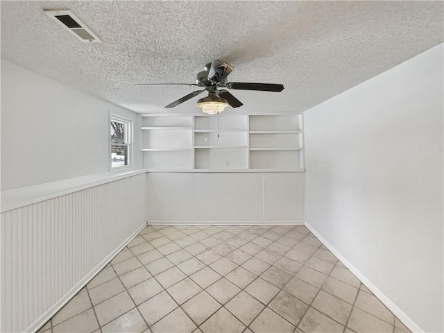 unfurnished room featuring visible vents, a textured ceiling, a wainscoted wall, and a ceiling fan