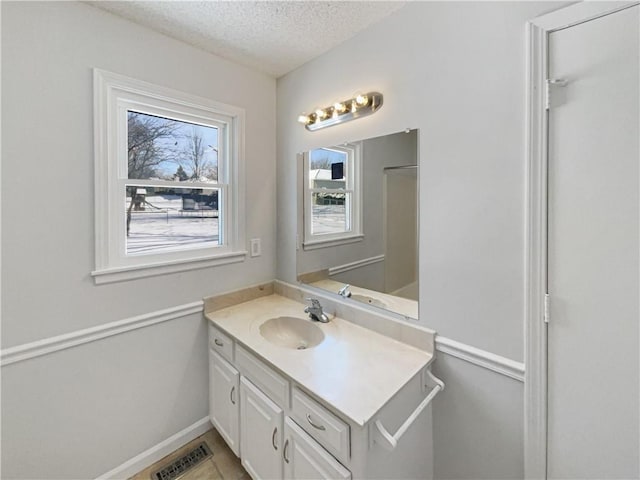 bathroom featuring vanity, baseboards, visible vents, and a textured ceiling