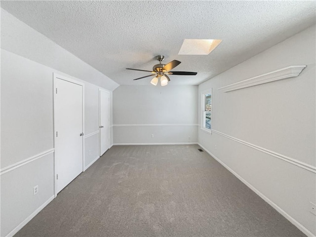 carpeted empty room featuring baseboards, a textured ceiling, a skylight, and ceiling fan