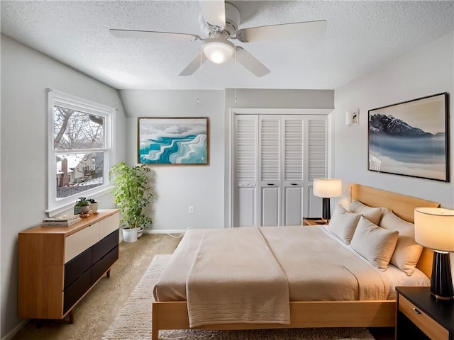 bedroom with baseboards, ceiling fan, light carpet, a closet, and a textured ceiling