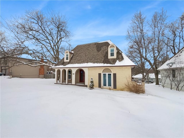 snow covered back of property featuring brick siding and roof with shingles