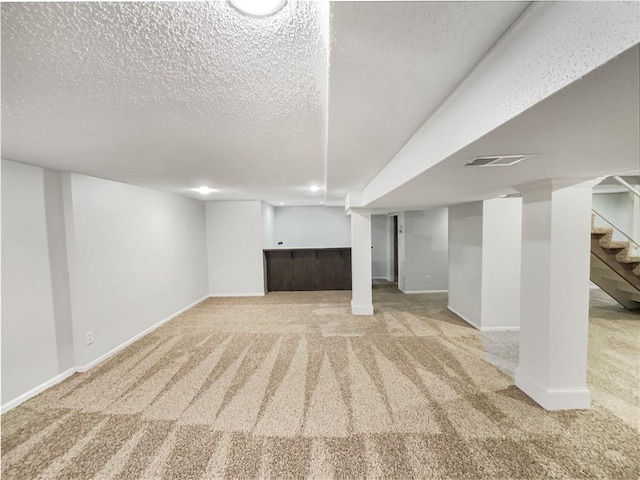 finished below grade area featuring carpet floors, a textured ceiling, and stairs