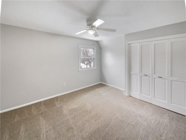 unfurnished bedroom with lofted ceiling, a closet, carpet, baseboards, and ceiling fan